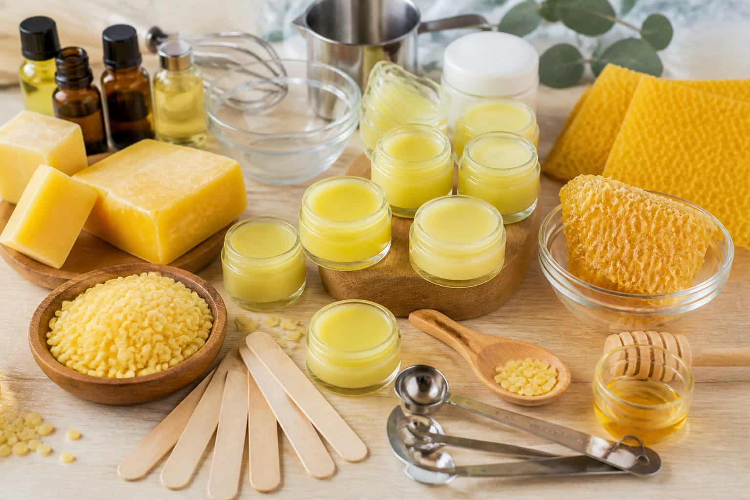 A workspace with beeswax, lip balm jars, wooden spatulas, and small containers arranged on a wooden table.