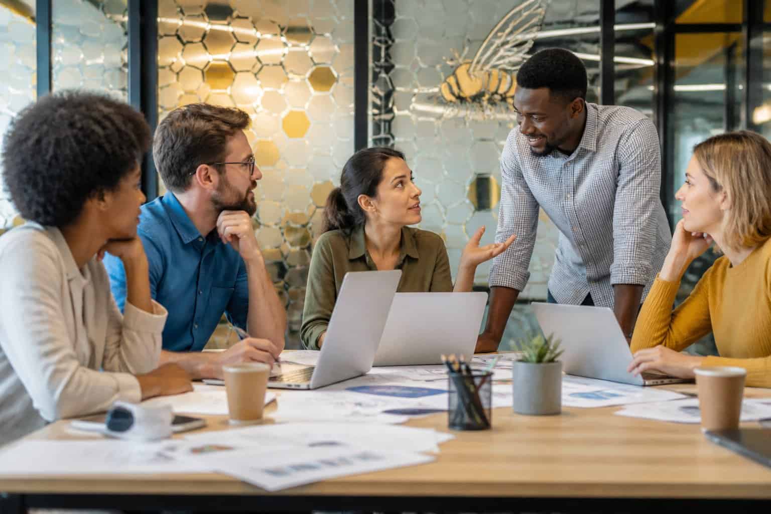 A group of people working together around a table in an office, discussing and collaborating with laptops and documents.