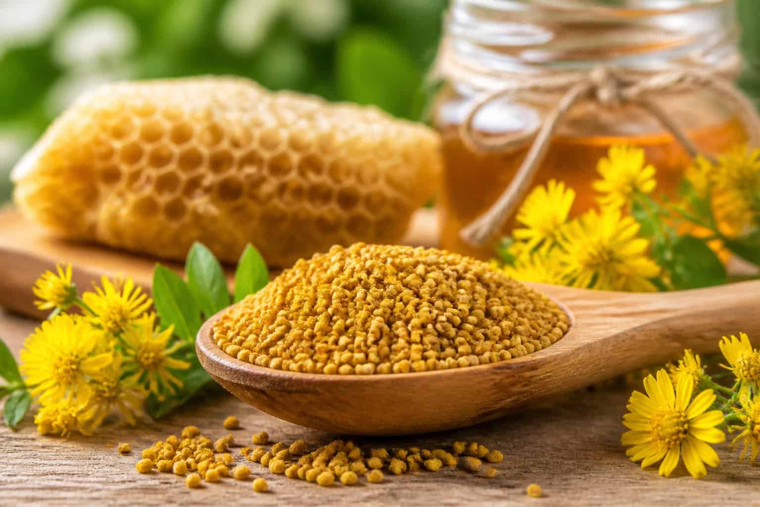 Close-up of a wooden spoon filled with bee pollen granules surrounded by yellow flowers and green leaves on a wooden surface.