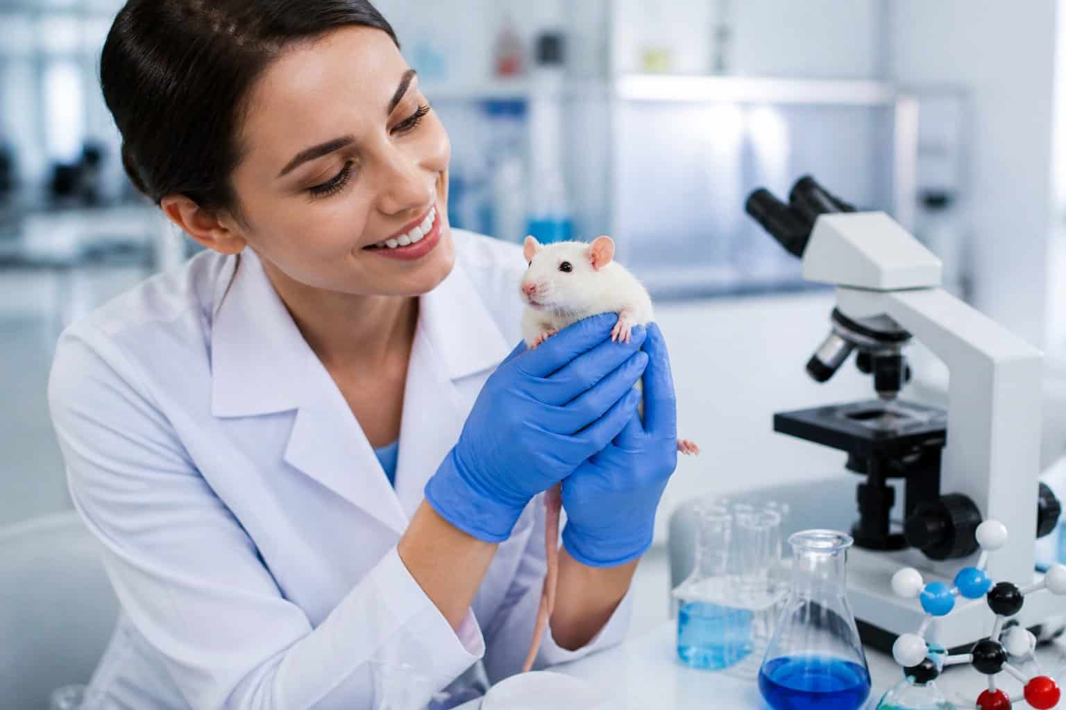 A scientist in a lab coat gently holding a laboratory rat inside a modern biomedical research lab.