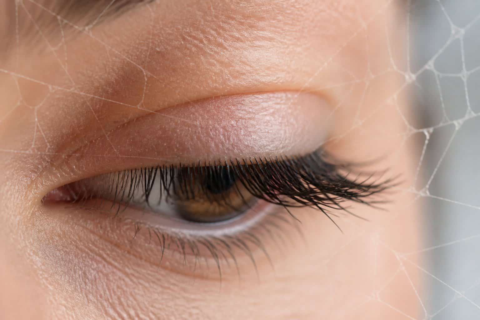 Close-up of a human eye blinking with faint spider web patterns overlaying the image.