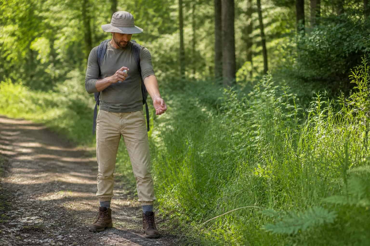 Hiker applying tick repellent while checking their arm on a woodland trail.